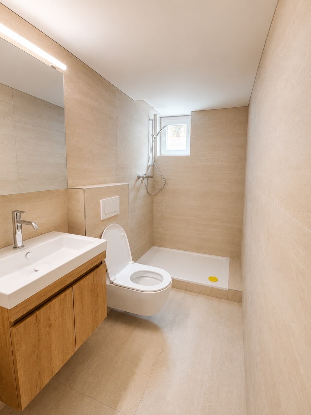 Badezimmer in Travertinoptik mit bodenebener Dusche, Holzwaschtisch und Wand-WC