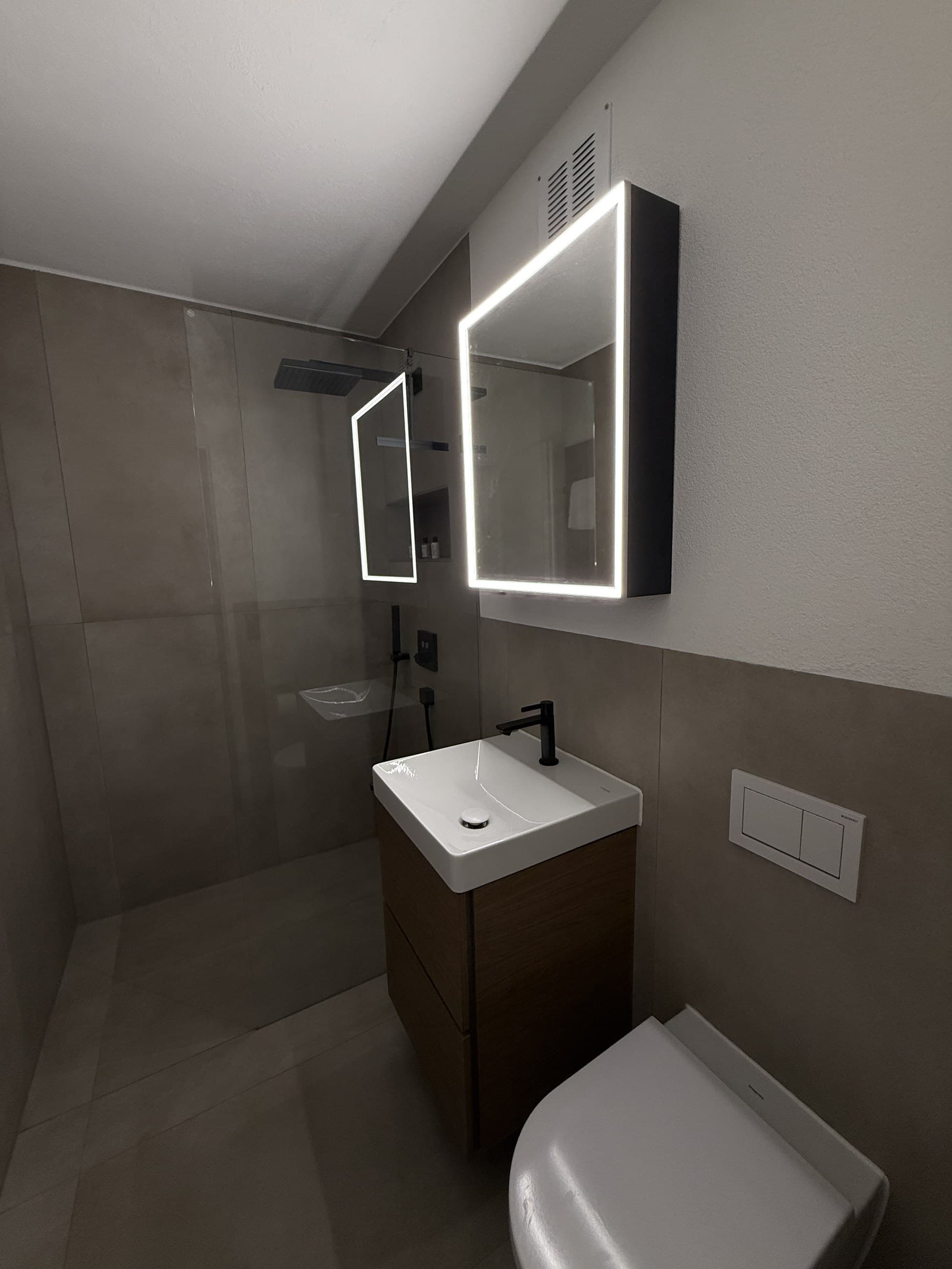 Badezimmer unter der Dachschräge mit grauen Grossformatplatten, LED-Spiegelschrank und Dusche