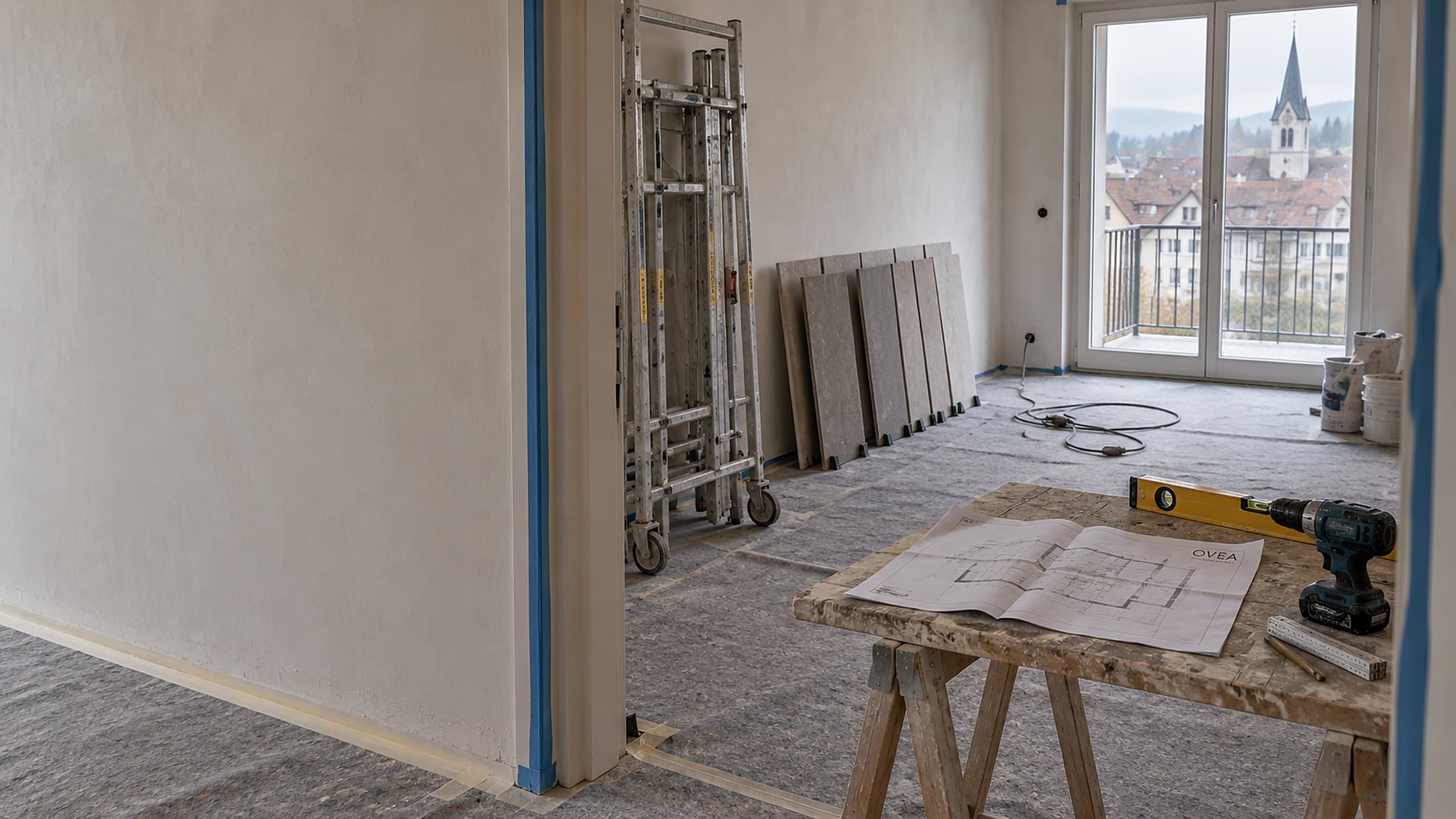 Wohnung mitten im Umbau, Boden mit Schutzvlies abgedeckt, Rollgerüst an der Wand, aufgestellte Grossformatplatten und ein Grundrissplan auf dem Holzbock